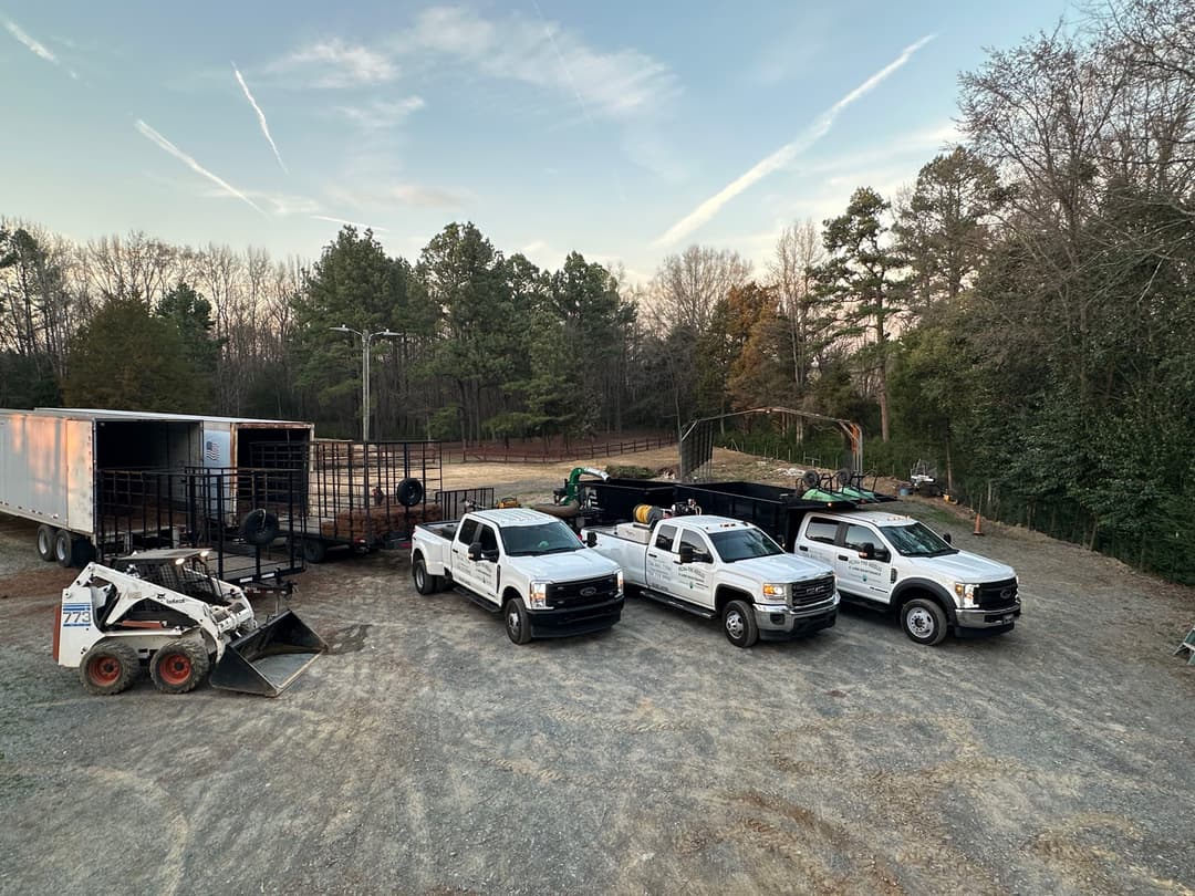 Trucks and equipment at a construction site surrounded by trees at sunset.