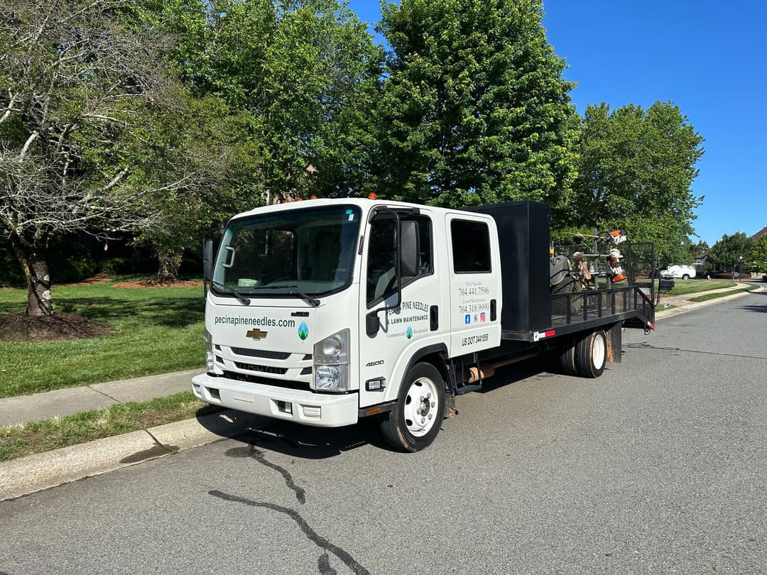Residential landscaping truck parked on a street with tools and equipment on the trailer.